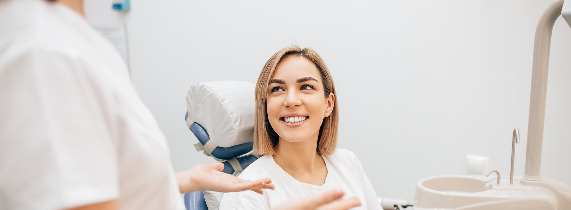 The image shows a woman sitting in a dental chair, receiving dental care from a professional wearing protective eyewear.