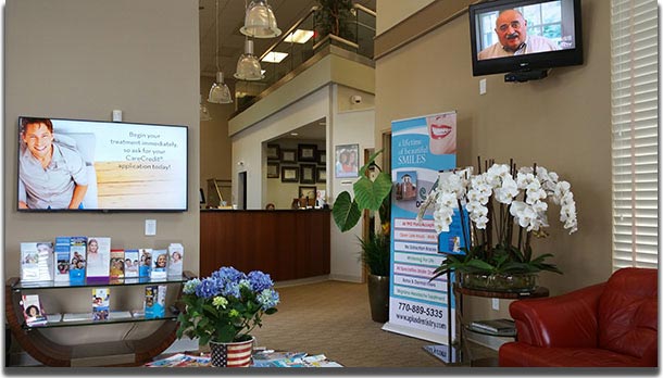 The image shows an interior view of a dental office waiting area with a television displaying a news program.