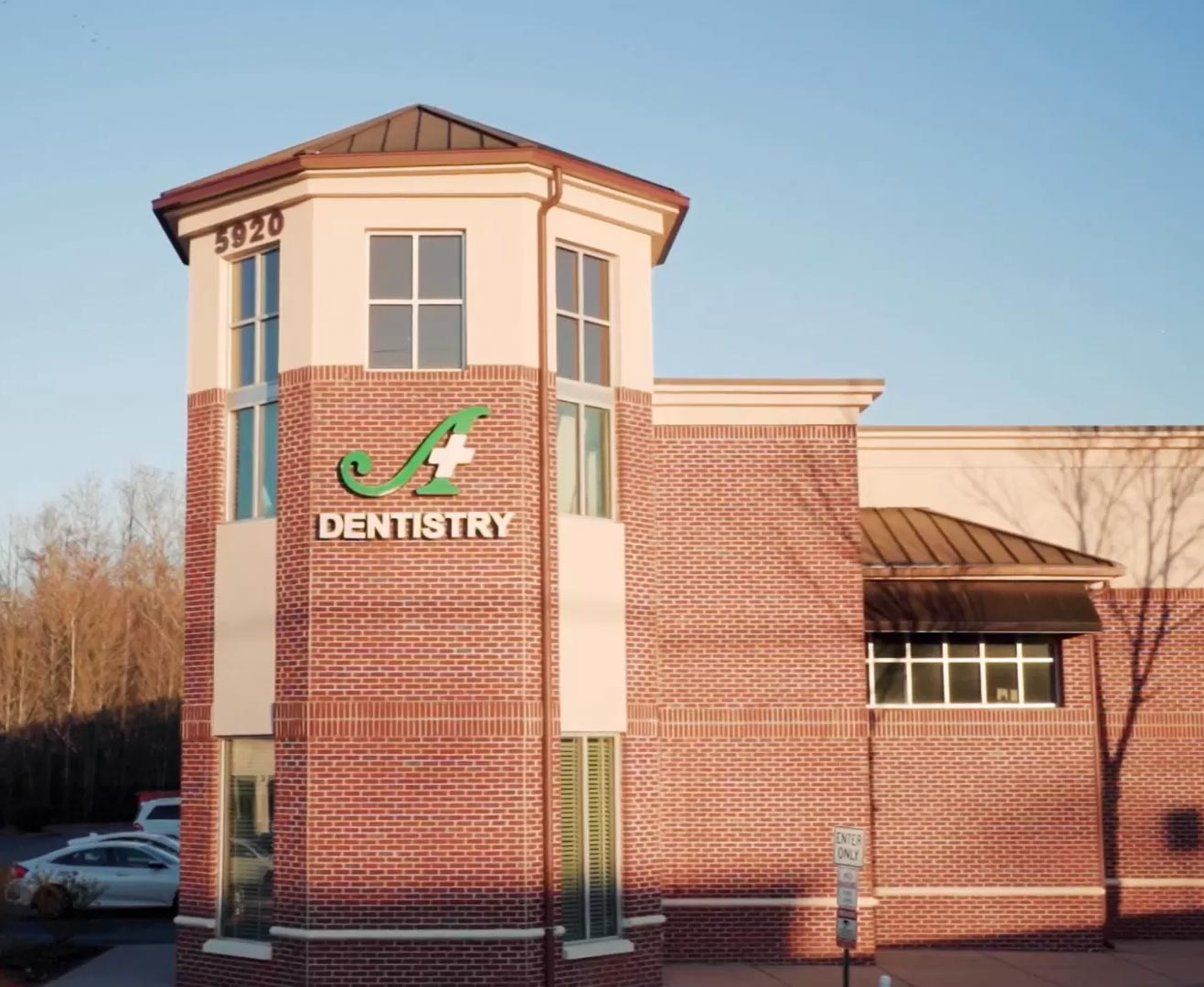 The image shows a brick building with a sign reading  Dentistry  on its facade, featuring a logo that appears to be a stylized letter  A  within a shield-like design, suggesting it is a dental clinic named  Dentistry.
