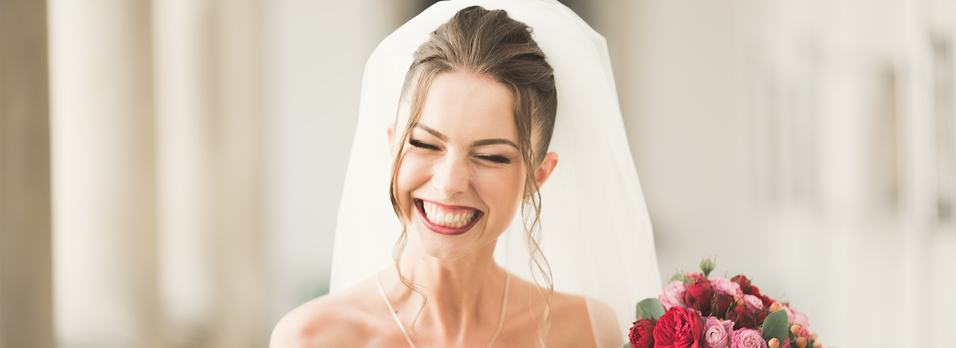 The image shows a bride and groom at their wedding, with the bride wearing a white dress and veil, and the groom in a suit, standing together under an archway, smiling and looking happy.
