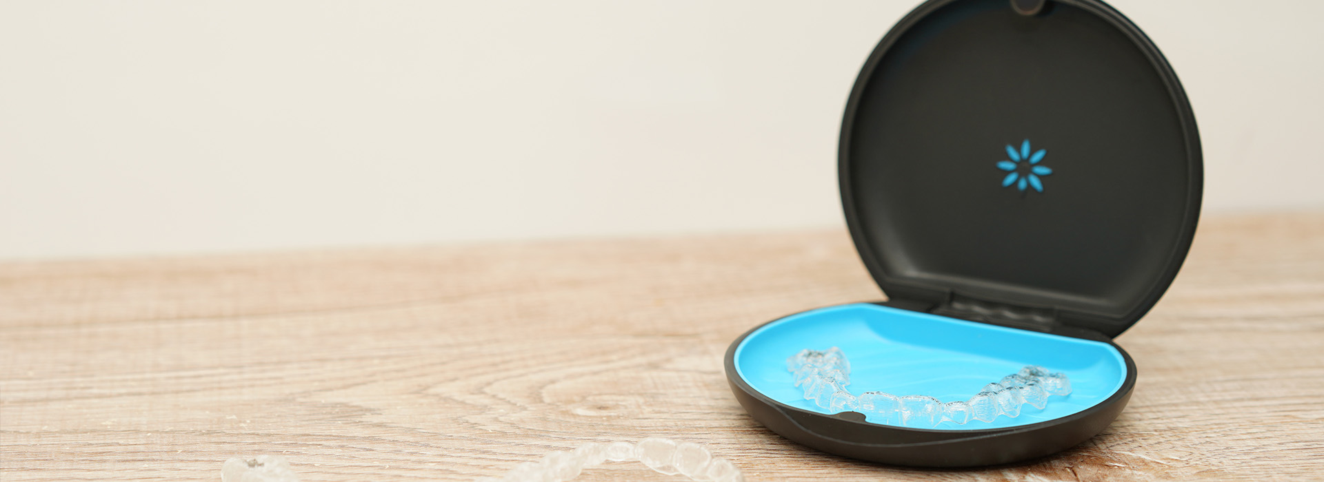 The image shows a small black case with a blue lid, possibly containing a product or accessory, placed on a wooden surface against a blurred background.