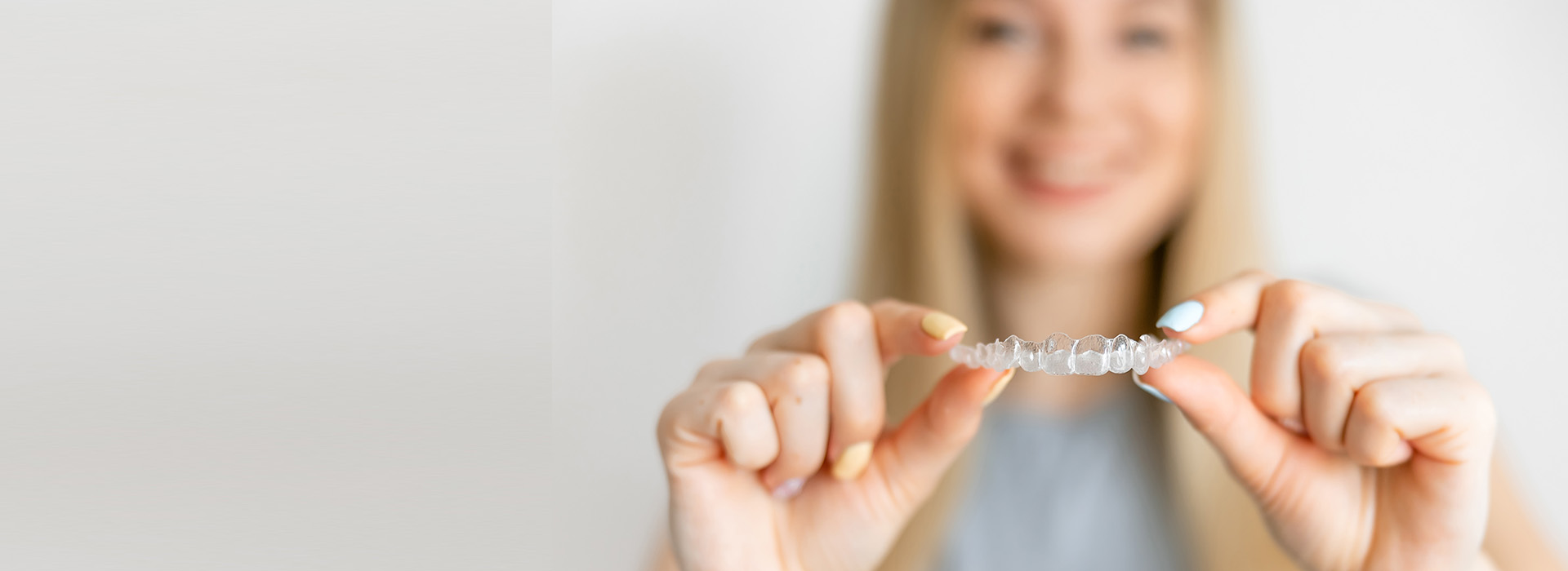 A woman holds a small object with both hands, positioned in front of her face, against a white background.