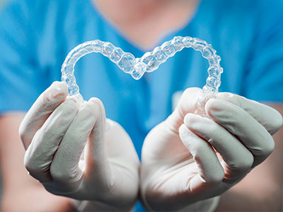 A person s hands holding a clear plastic heart-shaped object with a tooth-like texture, against a blue background.