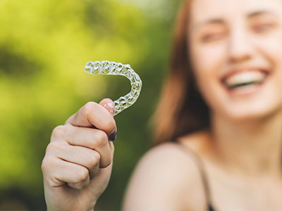 The image features a smiling individual holding up a toothbrush with a smiley face design.