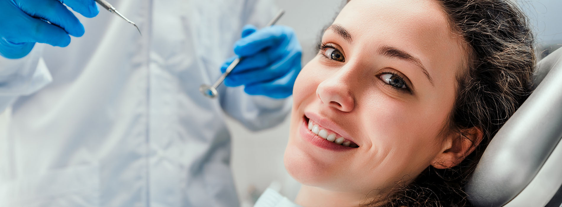 A smiling woman wearing blue scrubs with her eyes closed, surrounded by medical equipment, including a surgical table and instruments.