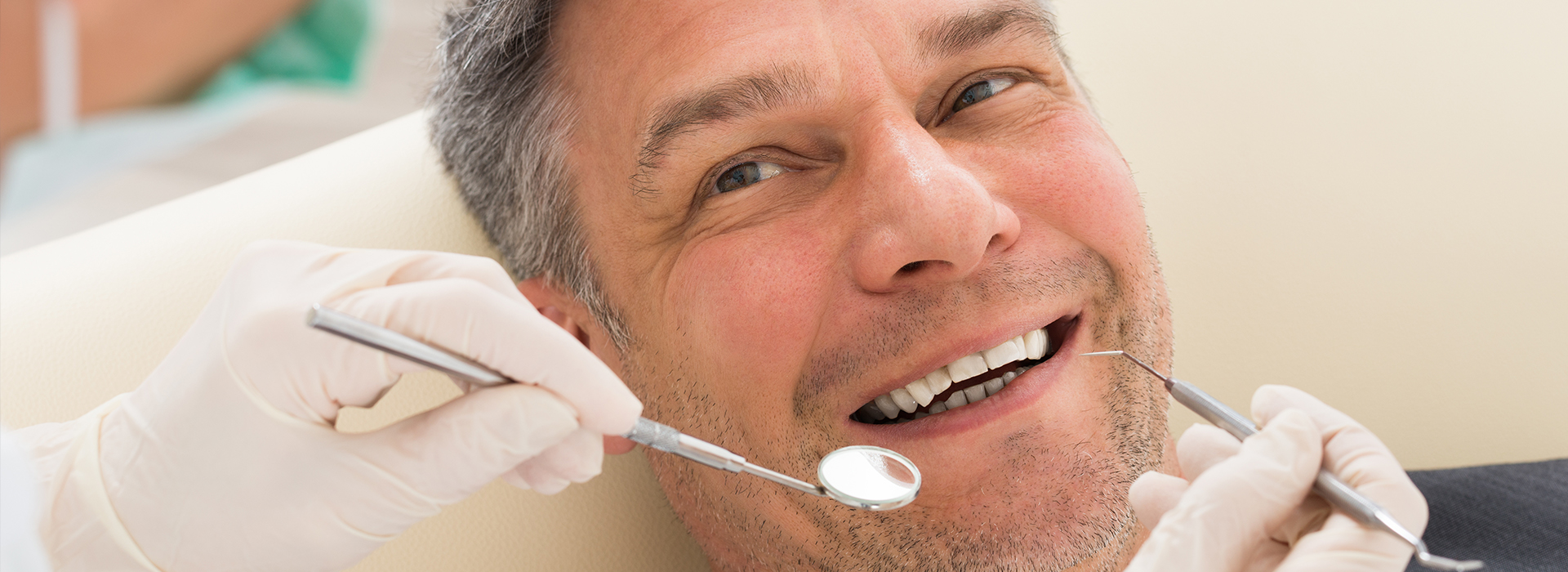 The image shows a man sitting in a dental chair with his mouth open, receiving dental treatment, with visible dental instruments being used on him by a professional.