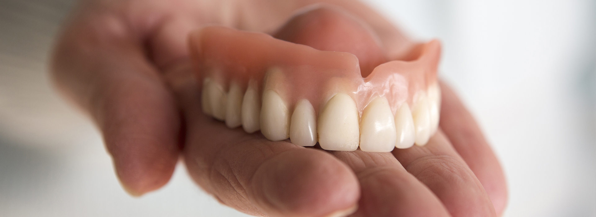 The image shows a person s hand holding an open mouth with artificial teeth, possibly for dental education or demonstration purposes.