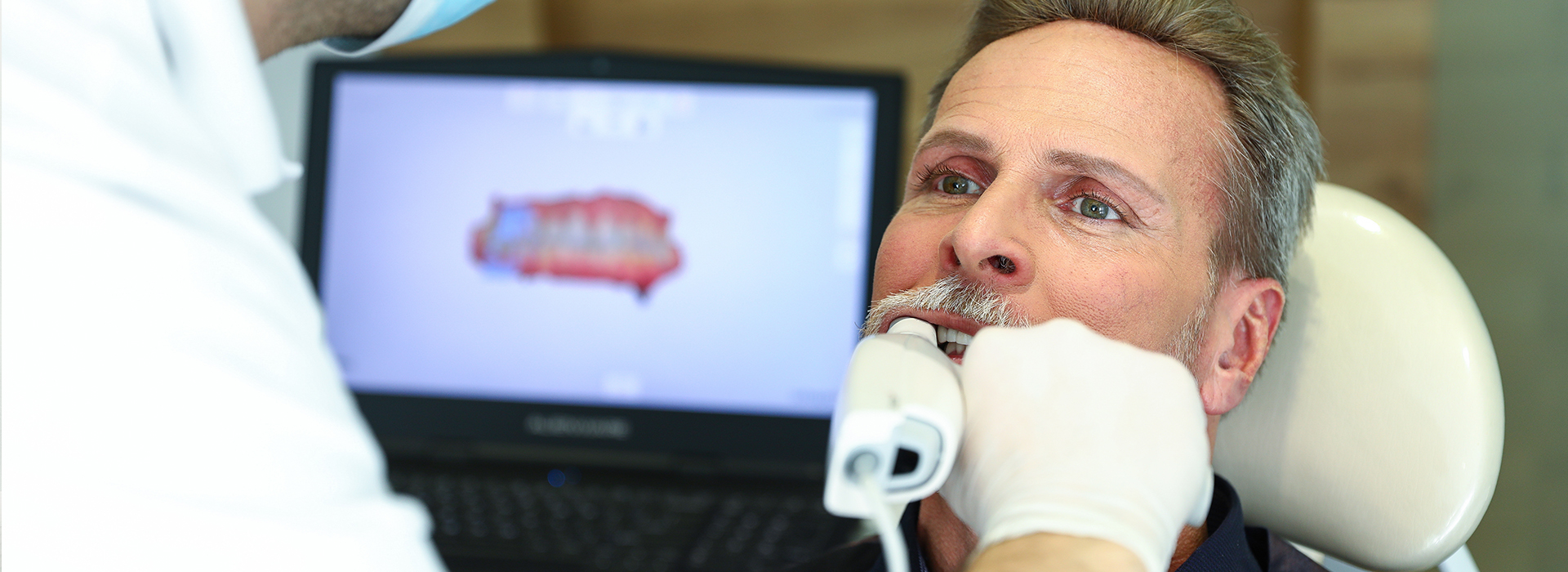 A dentist examining a patient s teeth with a large screen displaying an X-ray.