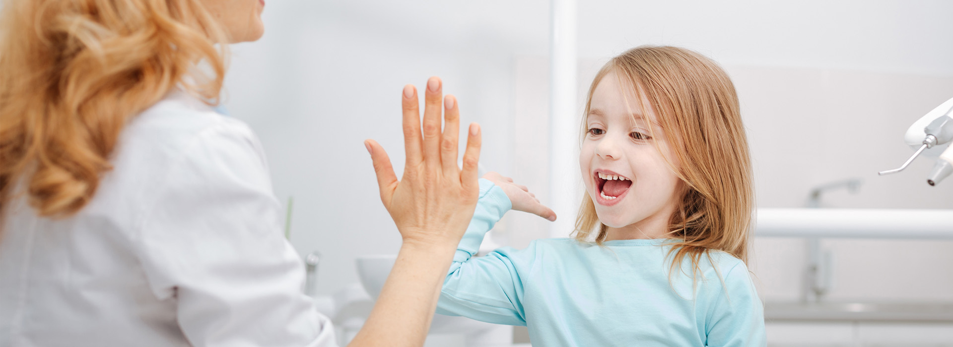A young girl with her hands raised high above her head, smiling at an adult who is clapping their hands.