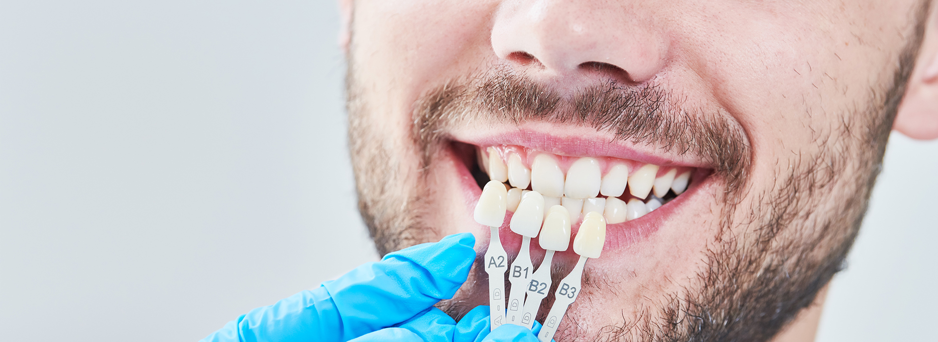 The image shows a person with a smile, holding a toothbrush towards their mouth, while wearing blue gloves and sitting in front of a mirror.