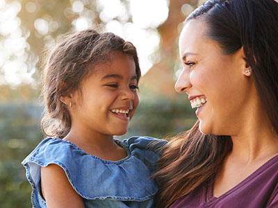 A woman and a child are smiling at each other outdoors during the daytime.