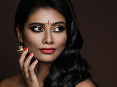 The image features a woman with dark hair and makeup, wearing a red lipstick, with her hand gently placed near her chin. She has a serious expression on her face.