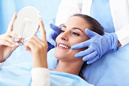 The image depicts a person lying on a medical table with a mirror held up to their face by two individuals wearing gloves, likely in a dental or medical setting.