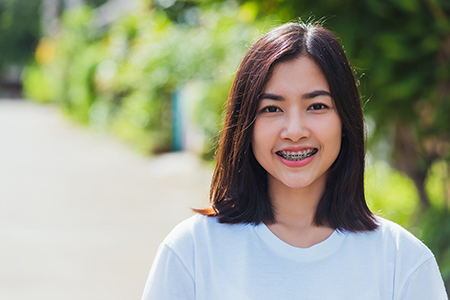 A young woman with short hair smiles at the camera, standing outdoors in front of a blurred background of greenery.