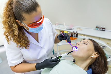 A dental hygienist using an electric toothbrush on a patient s teeth.