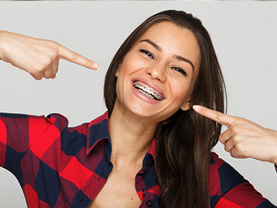 The image features a woman with a wide smile, pointing at her teeth, against a white background.