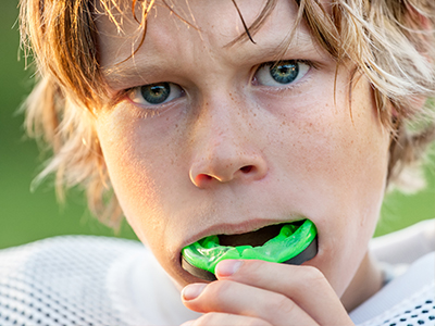 A young boy with blonde hair brushing his teeth while holding a toothbrush with green bristles.