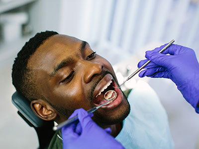 In the image, a person is seated with their mouth open while receiving dental treatment. A dental professional is performing the procedure using tools visible in the image.